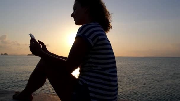Dziewczyna z telefonu komórkowego na plaży o zachodzie słońca. Zwolnionym tempie. — Wideo stockowe