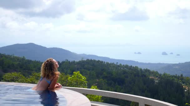Vrouw ontspannen in het zwembad genieten van uitzicht op zee — Stockvideo