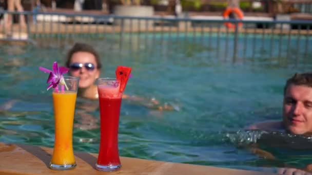 Jovem casal saudável que bebe sucos frescos na piscina — Vídeo de Stock