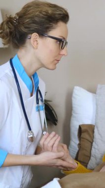 Kadın doktor, yaşlı bir hastanın elini nazikçe tutarak onu rahatlatıyor ve destekliyor. Bir ev ziyareti sırasında ya da bir bakımevinde şefkat ve bakım gösteren tıbbi uzmanlar