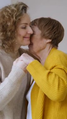 Yaşlı annesini sevgiyle kucaklayan kıvırcık saçlı yetişkin bir kızın şefkatli anı, sevgi, aile bağı, duygusal destek ve iki nesil arasındaki güçlü bağ.