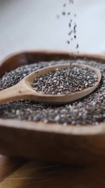 Besleyici siyah chia tohumları ağır çekimde bir kaşıkla ahşap bir kaseye düşüyor, süper yemek kavramını vurguluyor, sağlıklı beslenme, antioksidan faydaları ve bitki temelli diyet