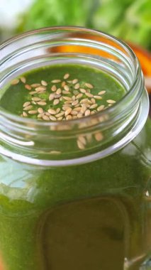 Dönen cam bir kavanozdaki besleyici yeşil detoks smoothie 'ye yakından bakın, susam tohumlarıyla süslenmiş, sağlıklı bir yaşam tarzı, vejetaryen diyeti ve organik yeme alışkanlıklarını teşvik ediyor.