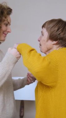 Yetişkin kızını sevmek yaşlı annelerinin ellerini nazikçe tutmak ve ona sımsıkı sarılmak, evde yaşayan iki nesil kadın arasında şefkat, şefkat ve güçlü aile bağları göstermek.