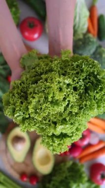 Avokado, domates, havuç ve brokoli de dahil olmak üzere çeşitli renkli sebzelerle güzel bir şekilde düzenlenmiş bir masaya taze bir baş marul düşüşü.