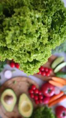 Sağlıklı bir yemek için domates, havuç ve avokado gibi çeşitli renkli sebzelerle dolu bir masanın üzerinde canlı yeşil bir demet marul tutan insanların ellerine yakın durun.