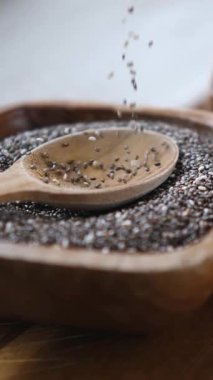 Yavaş çekim, sağlıklı chia tohumlarının yakın plan çekimi kasenin içindeki ahşap bir kaşığa düşerek besleyici süper yiyecekler ve sağlıklı organik malzemeler kavramını vurguluyor.