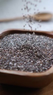 Yavaş çekim, kare bir ahşap kaseye düşen besleyici chia tohumlarını yakın çekim, sağlıklı beslenme, süper yiyecekler ve dengeli bir diyet için organik malzemeler kavramını vurguluyor.