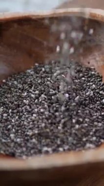 Besleyici siyah ve beyaz chia tohumları yavaş yavaş kırsal bir ahşap kaseye dökülüyor, sağlıklı beslenmede popüler olan bir süper besin maddesini sergiliyor, vegan diyetleri ve antioksidan faydaları için