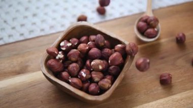 Kabuğu soyulmuş fındıklar ağır çekimde ahşap bir kaseye düşerek tahtanın üzerine yerleştirilmiş sağlıklı beslenme, organik malzemeler ve besleyici atıştırmalıklar konseptini gözler önüne seriyor.