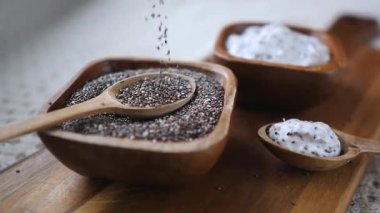 Chia tohumları yavaş yavaş bir kaşık ile ahşap bir kaseye dökülüyor, kahvaltılık puding için sağlıklı bir süper gıda bileşenini vurguluyor, besleyici, organik ve vejetaryen bir yaşam tarzını teşvik ediyor.