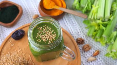 Sağlıklı yeşil smoothie, ahşap bir tabakta dönen, çevresi kereviz, spirulina, zerdeçal, fındık ve susam tohumlarıyla çevrili besleyici bir vejetaryen kahvaltısı için