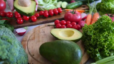 İnsanlar, sağlıklı bir vejetaryen yemeği için ahşap kesme tahtasındaki renkli organik sebzelerle çevrili yeni dilimlenmiş avokado yarısından büyük bir tohum alıyorlar.