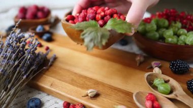 İnsanlar ahşap bir kase taze yabani çileği kesme tahtasına dikkatlice yerleştirir, ahududu, yabanmersini, bektaşi üzümü ve kırmızı üzümlerden oluşan güzel bir çeşitliliğe katılır.