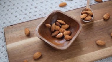 Kesme tahtasına yerleştirilmiş güzel bir ahşap kaseye dökülen çiğ bademlerin yavaş çekim görüntüleri sağlıklı atıştırmalıkların ve doğal organik gıdaların mükemmel bir temsili.