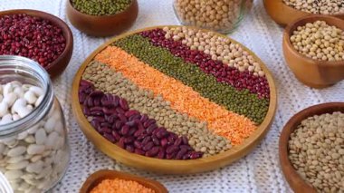 Fasulye, mercimek, nohut ve soya fasulyesi gibi çeşitli ham baklagiller, ahşap kaseler ve bitki temelli zengin bir protein kaynağını ön plana çıkaran merkezi bir tabakta güzelce düzenlenmiştir.