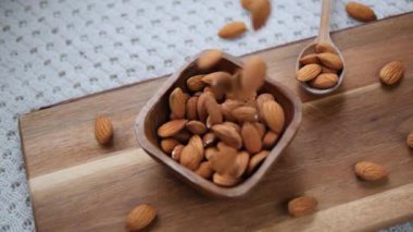 Kavrulmuş bademler yavaş yavaş yukarıdan kırsal ahşap bir kaseye dökülüyor. Sağlıklı bir yaşam tarzını, süper beslenme tarzını ve organik vejetaryen atıştırmalarını temsil ediyor.