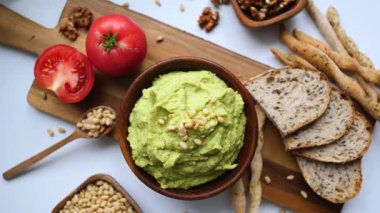 Lezzetli ve sağlıklı bir aperatifin üst görüntüsünde bir kase taze avokado guacamole soslu çam fıstığı serpiştirilmiş, domates, ceviz ve tam tahıllı ekmek çubukları ile servis edilir.