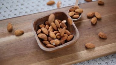 Organik çiğ badem fıstıkları, küçük bir tahta kaseye düşüp, sağlıklı bir yaşam tarzını, bitki temelli diyeti ve protein açısından zengin, besleyici vejetaryen atıştırmalıkları temsil ediyor.