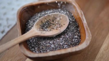 Besin zengini chia çekirdeklerini kapayarak ahşap bir kaşığın içine düşüyorlar ve kırsal bir kasede dinleniyorlar. Sağlıklı beslenme ve vejetaryen yaşam tarzlarında popüler bir süper yiyecek içeriği sergiliyorlar.