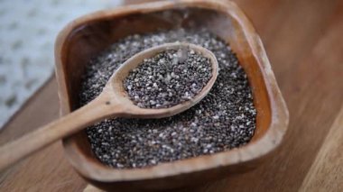 Çiğ chia tohumlarının üst görüntüsü yavaşça ahşap bir kaşıktan kırsal bir kaseye düşüyor, sağlıklı bir diyet, süper yiyecek ve sağlıklı olmak için organik doğal bileşenleri vurguluyor.