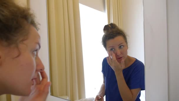 Женщина намазывает лицо кремом от старения — стоковое видео
