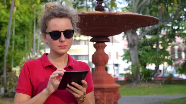 Νεαρή γυναίκα χρησιμοποιώντας δισκίο υπαίθρια στο πάρκο — Αρχείο Βίντεο
