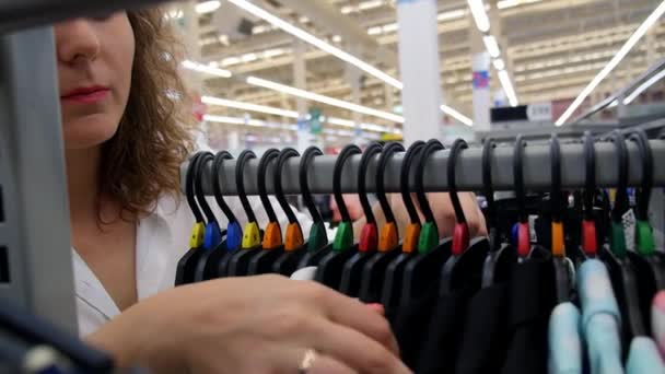 Женщина выбирает платье во время покупок в магазине одежды — стоковое видео