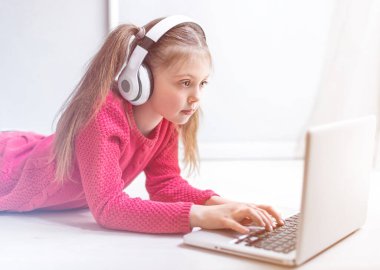 Kulaklık takan sevimli küçük kız evde online eğitim, ev eğitimi ve internet iletişimi için dizüstü bilgisayar kullanıyor. Çocuklar uzaktan öğreniyor. Sosyal mesafe. Evde kal..