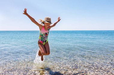 Çocuk yazın sahildeki dalgalarda mutlu bir şekilde zıplar ve kameraya bakar. Metin için alanı kopyala