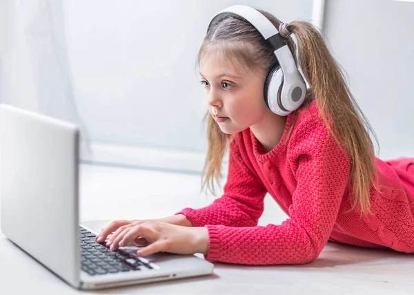 Kulaklık takan sevimli küçük kız evde online eğitim, ev eğitimi ve internet iletişimi için dizüstü bilgisayar kullanıyor. Çocuklar uzaktan öğreniyor. Sosyal mesafe. Evde kal..