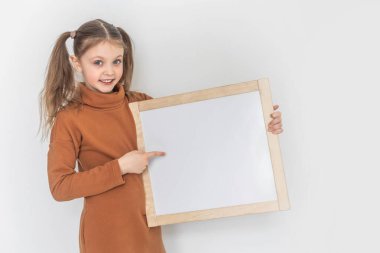 Mutlu gülümseyen kız boş bir çizim tahtası tutuyor işaret parmağıyla yönü gösteriyor. Beyaz arkaplan üzerinde test için alanı kopyala