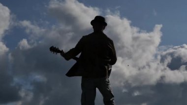 adam gitar arkadan görünüm karşı güneşin ve bulutların yavaş odaklanmak takip ile