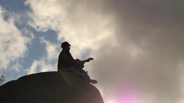 El hombre con la guitarra contra el sol en el acantilado de cámara lenta sigue el enfoque — Vídeos de Stock