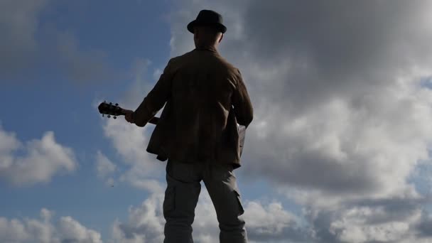 Άνθρωπος με κιθάρα ΠΙΣΩ ΟΨΗ ενάντια σε αργή κίνηση νεφώσεις και ήλιος — Αρχείο Βίντεο