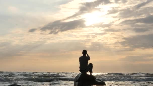 Silueta muže na skále v rozbouřeném moři modlit, aby slunce žádá o pomoc dolly shot — Stock video