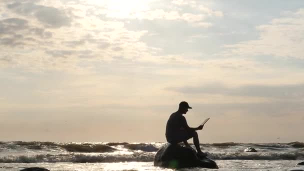 İlginç bir kitap - rock güneş dolly atış karşı fırtınalı denizde okuma adam — Stok video