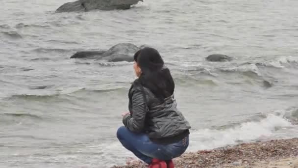 Woman at sea line throwing pebbles to a water — Stock Video