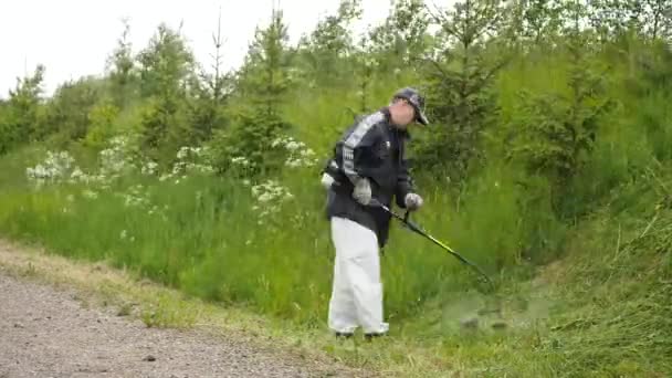 Mann mäht mit Kraftstofftrimmer im Zeitraffer das grüne Gras am Hang ab — Stockvideo