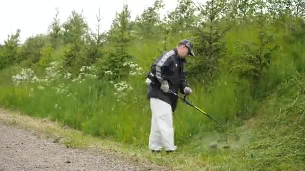 Man klipper ner det gröna gräset på sluttning med bränsle trimmer tidsinställd — Stockvideo