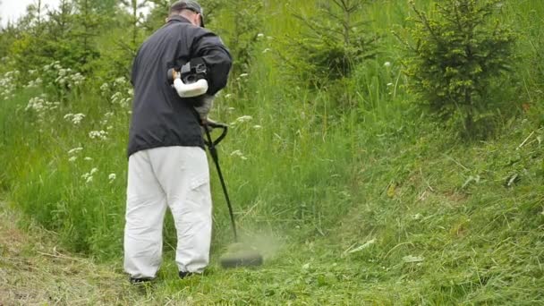 Mens neer op helling met brandstof rietenknipper slow motion het groene gras maaien — Stockvideo
