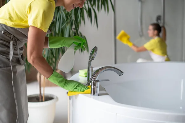 Professional cleaning of the bathroom and toilet. Cleanliness and hygiene at home. Cleaning service and housekeeping. Hand in green and yellow latex gloves. Rubbing the bathroom and taps