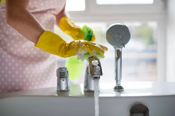 Professional cleaning of the bathroom and toilet. Cleanliness and hygiene at home. Cleaning service and housekeeping. Hand in green and yellow latex gloves. Rubbing the bathroom and taps