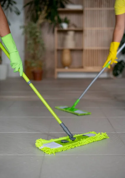 A professional cleaners wash the floor with a two mops. A green rag rubs the floor. Cleaning of apartments and premises. Cleaning equipment and supplies