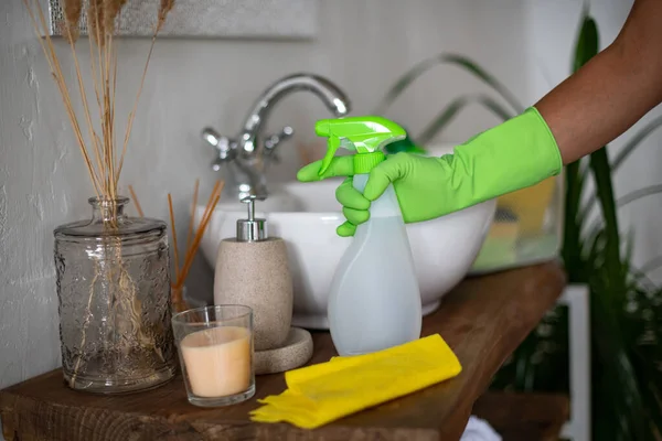 Cleaning the bathroom. The girl rubs the sink and mirror. Hotel service. Professional cleaning of apartments and premises. Yellow and green uniforms. Rubber gloves, apron and cleaning supplies