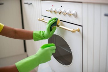 Mutfağın genel temizliği. Önlüklü ve lastik eldivenli bir kadın lavaboyu yıkıyor. Profesyonel ev işi. Fırını paçavrayla temizliyorum.