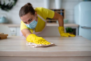 Profesyonel temizlik servisi, oda servisi. Mutfakta hijyen ve temizlik var. Sarı eldivenli bir temizlikçi kadın duvardaki tozu siliyor. Çalışan el