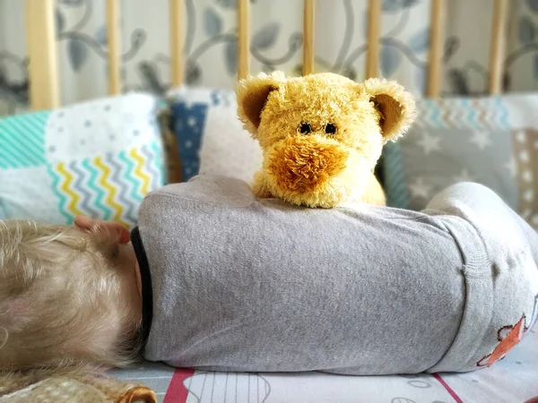 A little boy sleeps in a crib and a teddy bear protects him — Stock Photo, Image