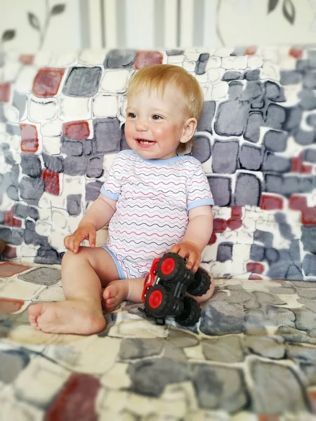 Feliz riendo un niño de un año en un sofá ligero jugando con un coche de juguete —  Fotos de Stock