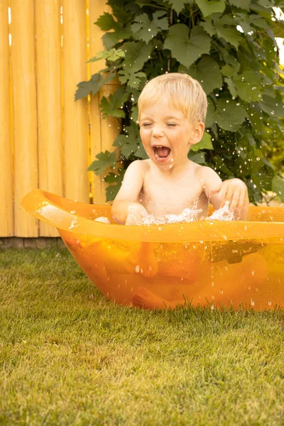 Ein kleiner Junge planscht im Sommer im Kinderbad auf dem Rasen — Stockfoto